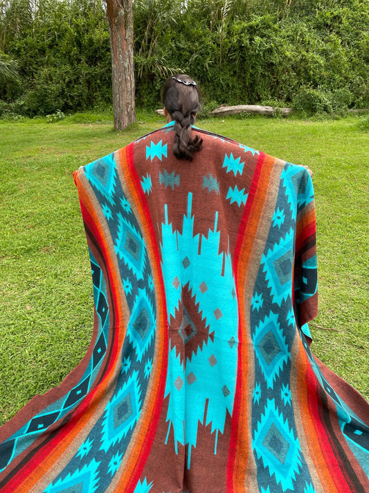 TomHats alpaca wool blanket with a turquoise and brown Navajo pattern, held by a person outdoors.