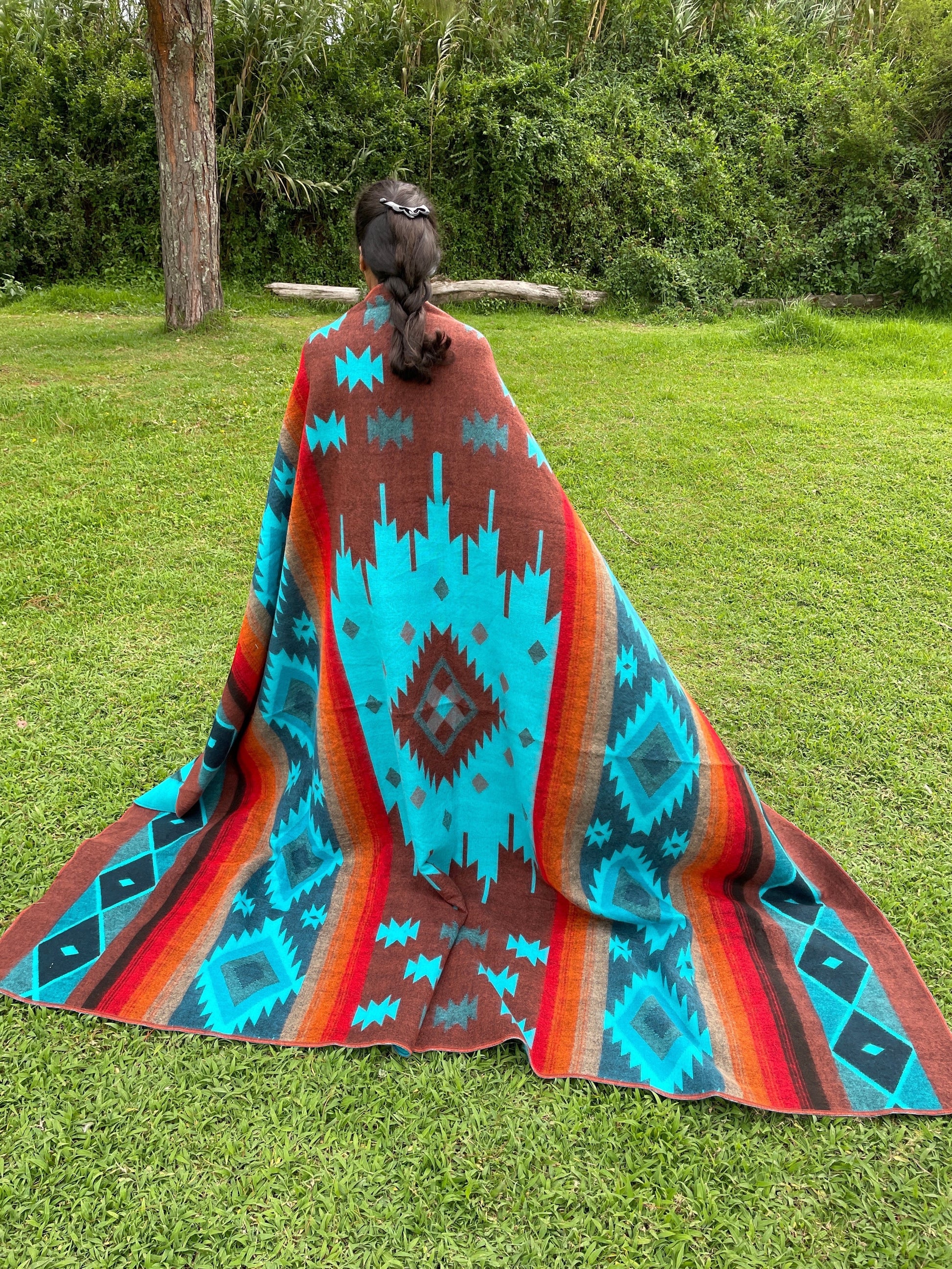 TomHats alpaca wool blanket with a turquoise and brown Navajo pattern, held by a person outdoors.