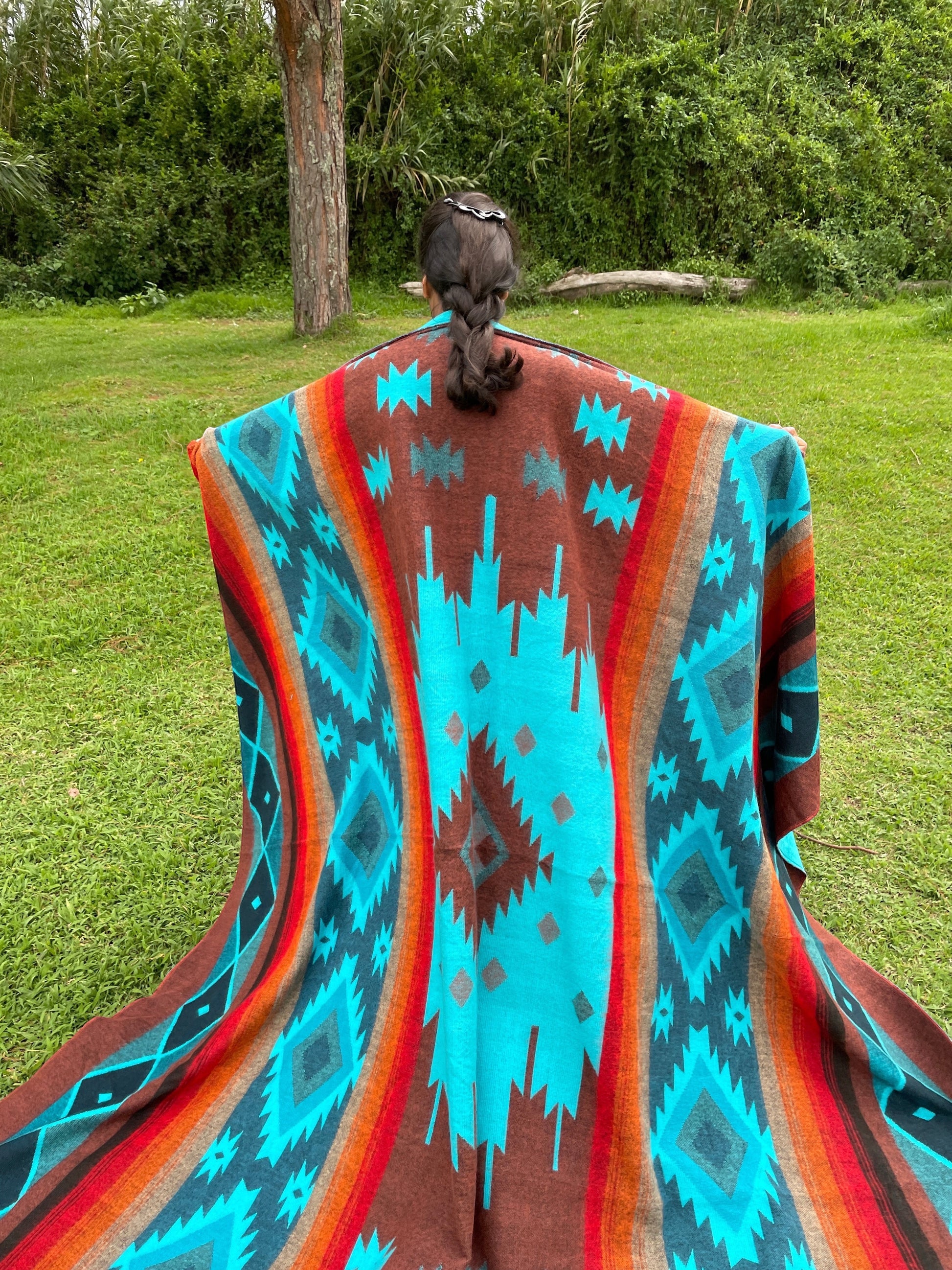 TomHats alpaca wool blanket with a turquoise and brown Navajo pattern, held by a person outdoors.