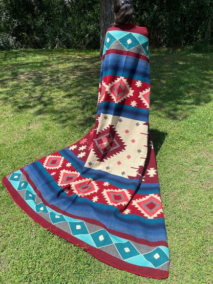 TomHats alpaca wool blanket with traditional Navajo patterns in red and blue on a green meadow.
