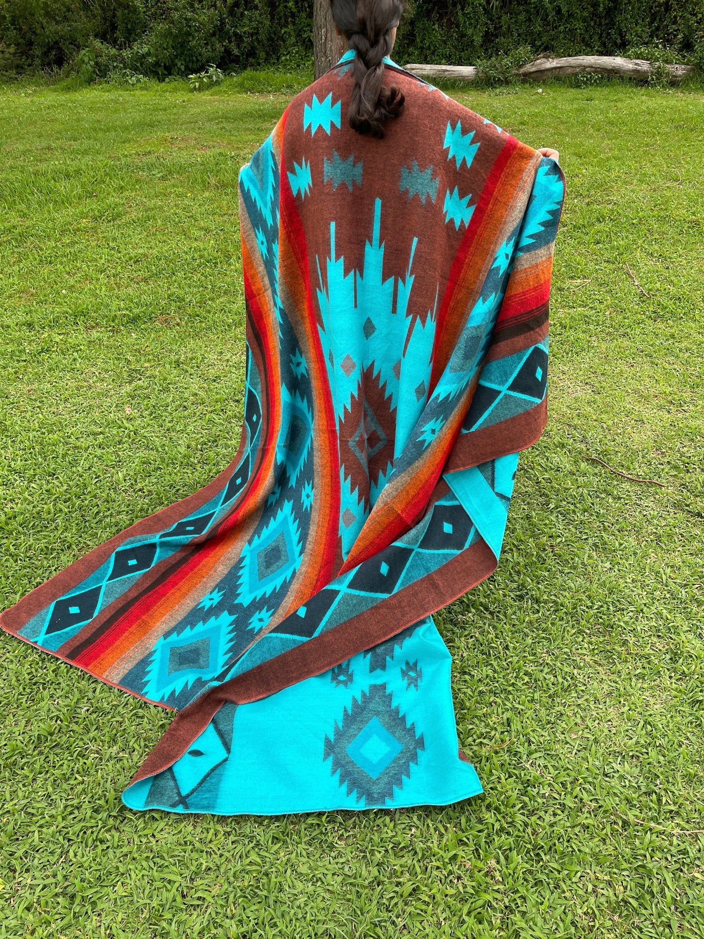 TomHats alpaca wool blanket with a turquoise and brown Navajo pattern, held by a person outdoors.