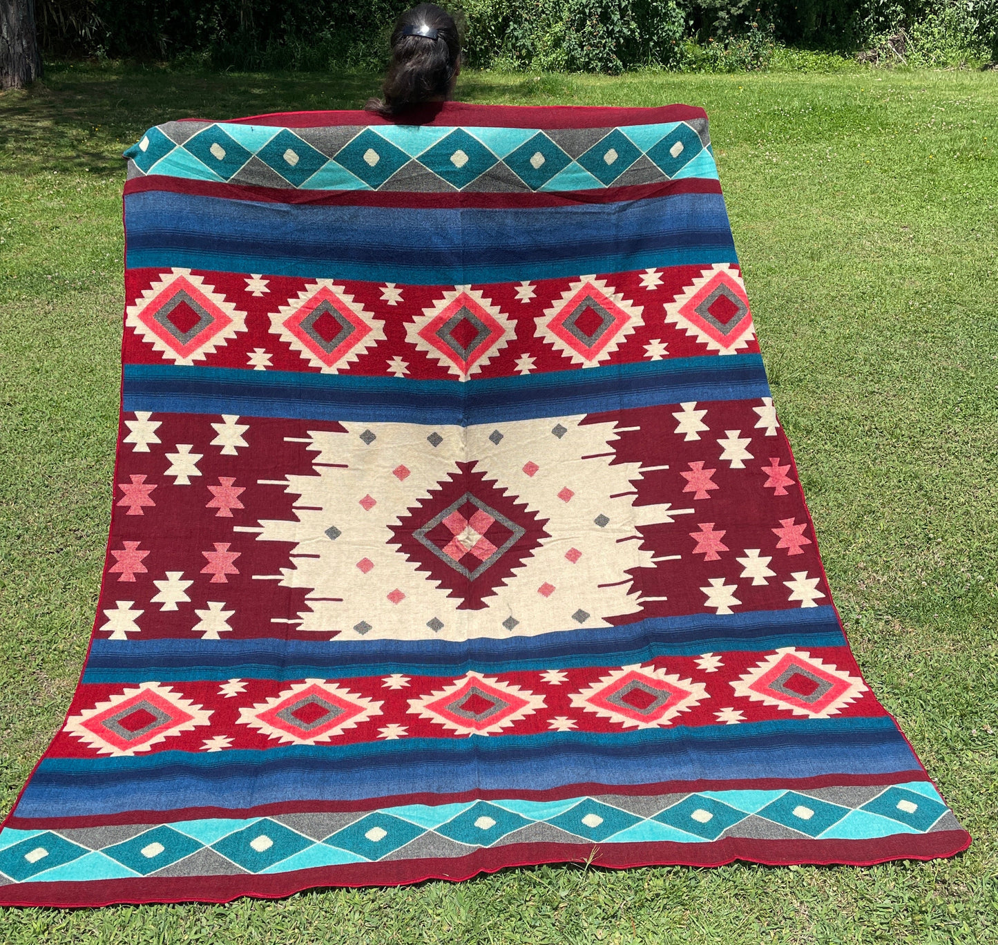 TomHats alpaca wool blanket with traditional Navajo patterns in red and blue on a green meadow.