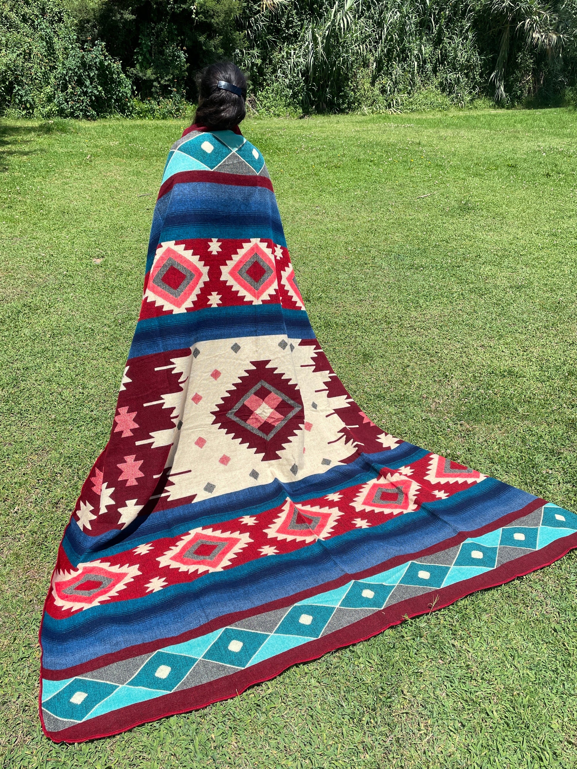 TomHats alpaca wool blanket with traditional Navajo patterns in red and blue on a green meadow.