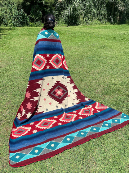 TomHats alpaca wool blanket with traditional Navajo patterns in red and blue on a green meadow.