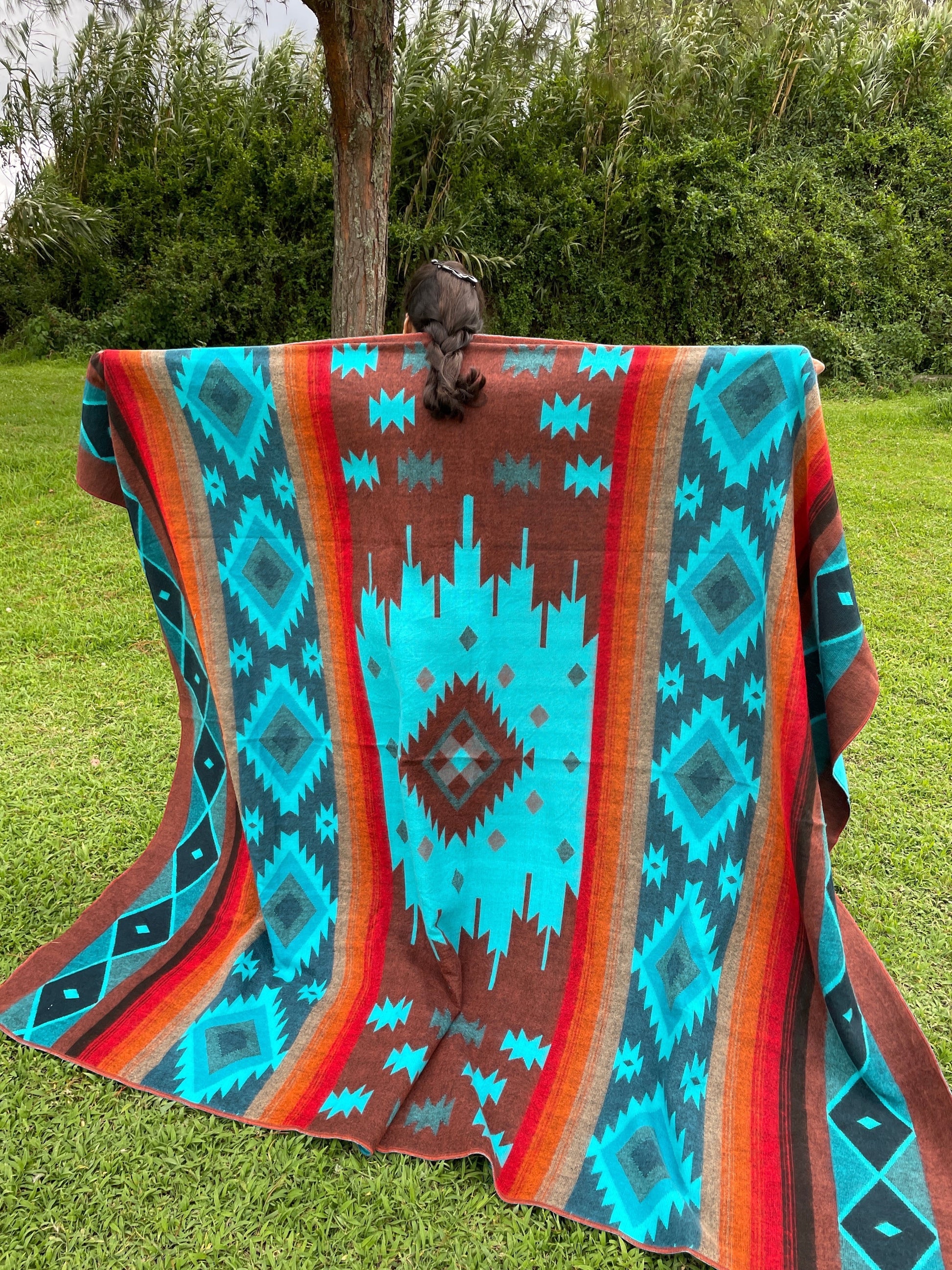 TomHats alpaca wool blanket with a turquoise and brown Navajo pattern, held by a person outdoors.