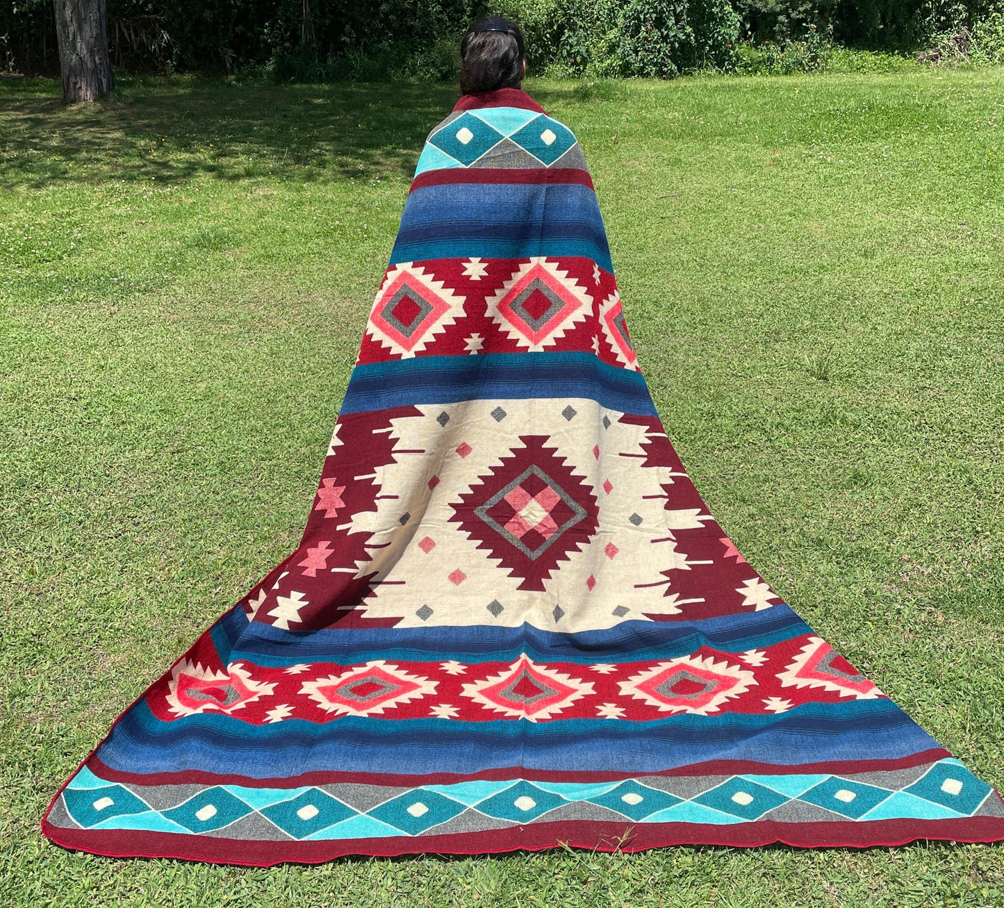 TomHats alpaca wool blanket with traditional Navajo patterns in red and blue on a green meadow.