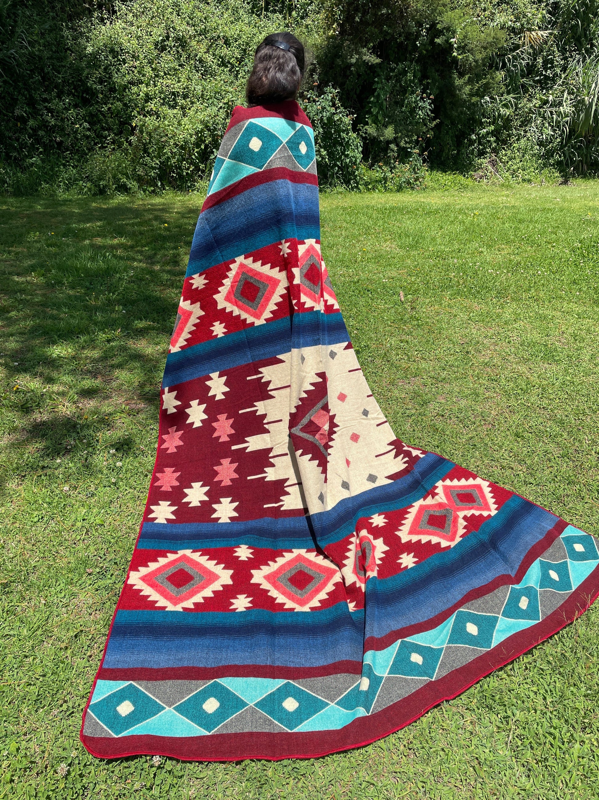 TomHats alpaca wool blanket with traditional Navajo patterns in red and blue on a green meadow.