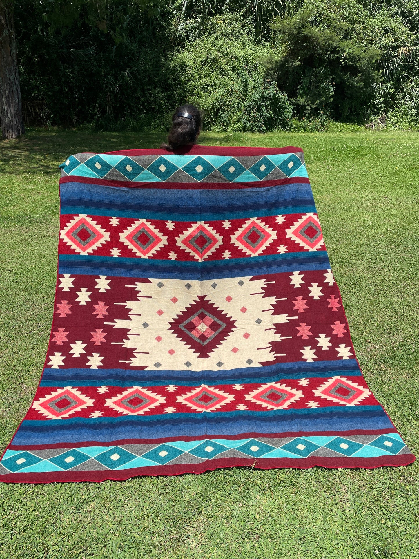 TomHats alpaca wool blanket with traditional Navajo patterns in red and blue on a green meadow.
